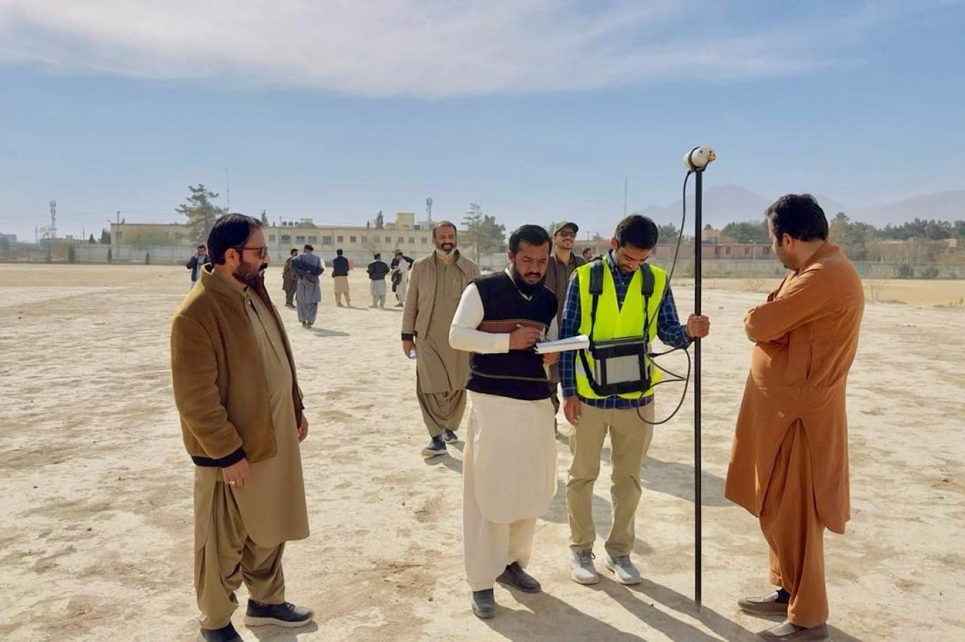Geologists and officials inspecting mineral exploration equipment in an open land field in Balochistan.