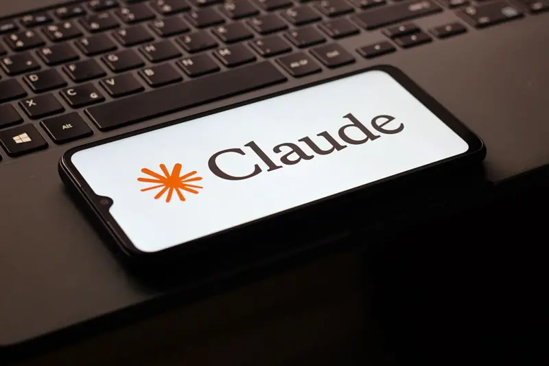 A smartphone lying on a laptop keyboard displaying the Anthropic Claude AI logo on its screen.